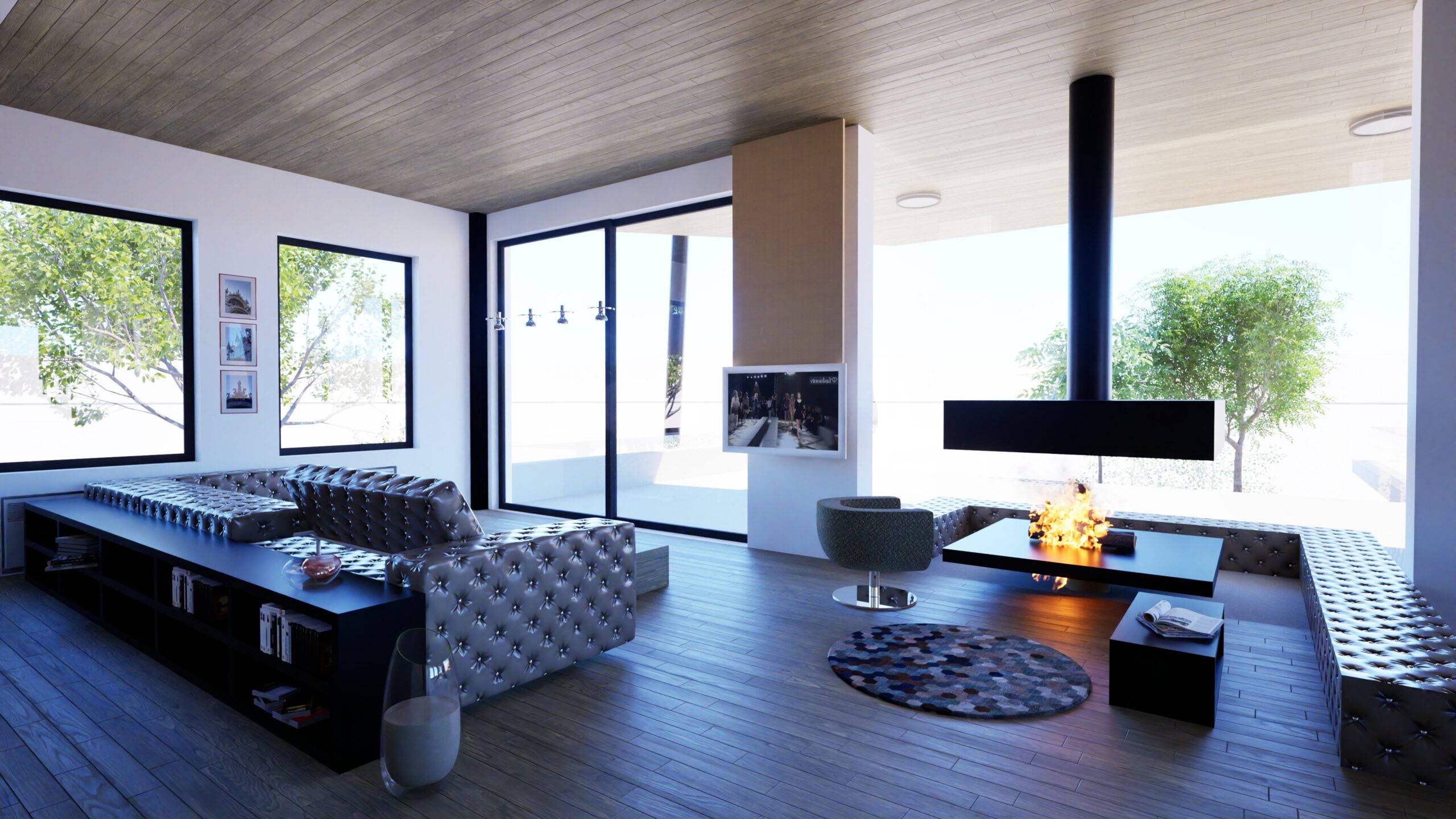 A spacious, modern living room with a long, tufted grey sofa, a suspended fireplace, and large windows offering views of lush greenery. The room features a wood plank ceiling, dark wood flooring, and a mix of contemporary furniture, including a round rug and a green accent chair. A glass of milk sits on a low table, adding a touch of domesticity to the sleek design. By Modify Architects